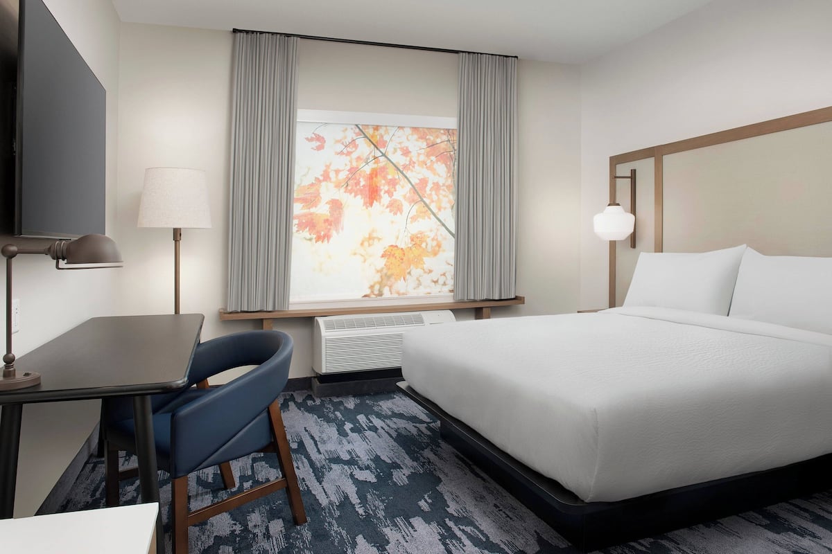 A hotel room with a bed, a desk, a chair, a lamp, and a window with curtains.
