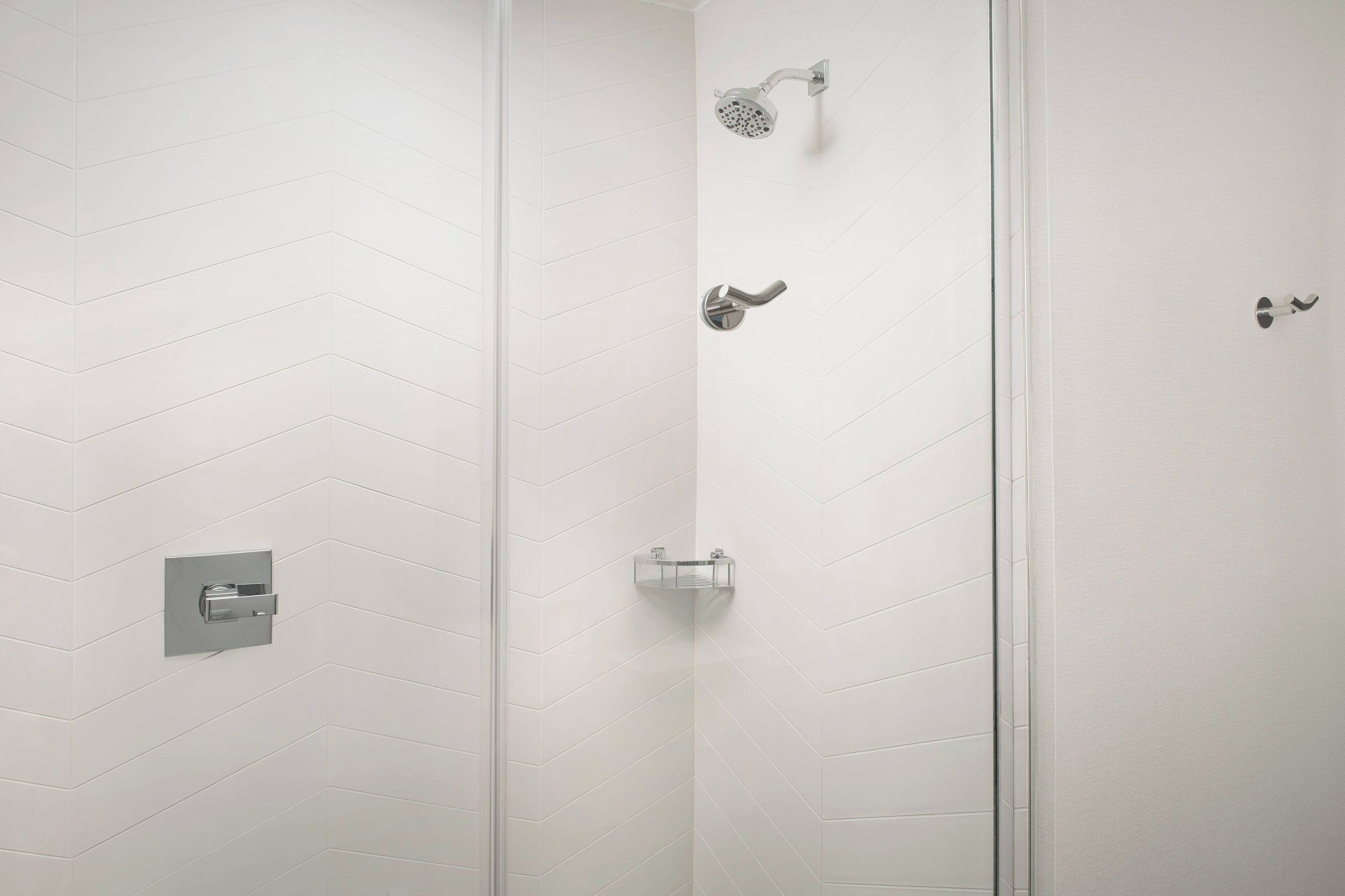 A shower area with a white tiled wall, a showerhead, and a handheld showerhead.