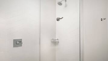 A shower area with a white tiled wall, a showerhead, and a handheld showerhead.