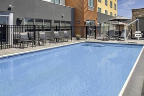 A swimming pool with a black metal fence, outdoor seating with chairs and a table, and a potted plant.