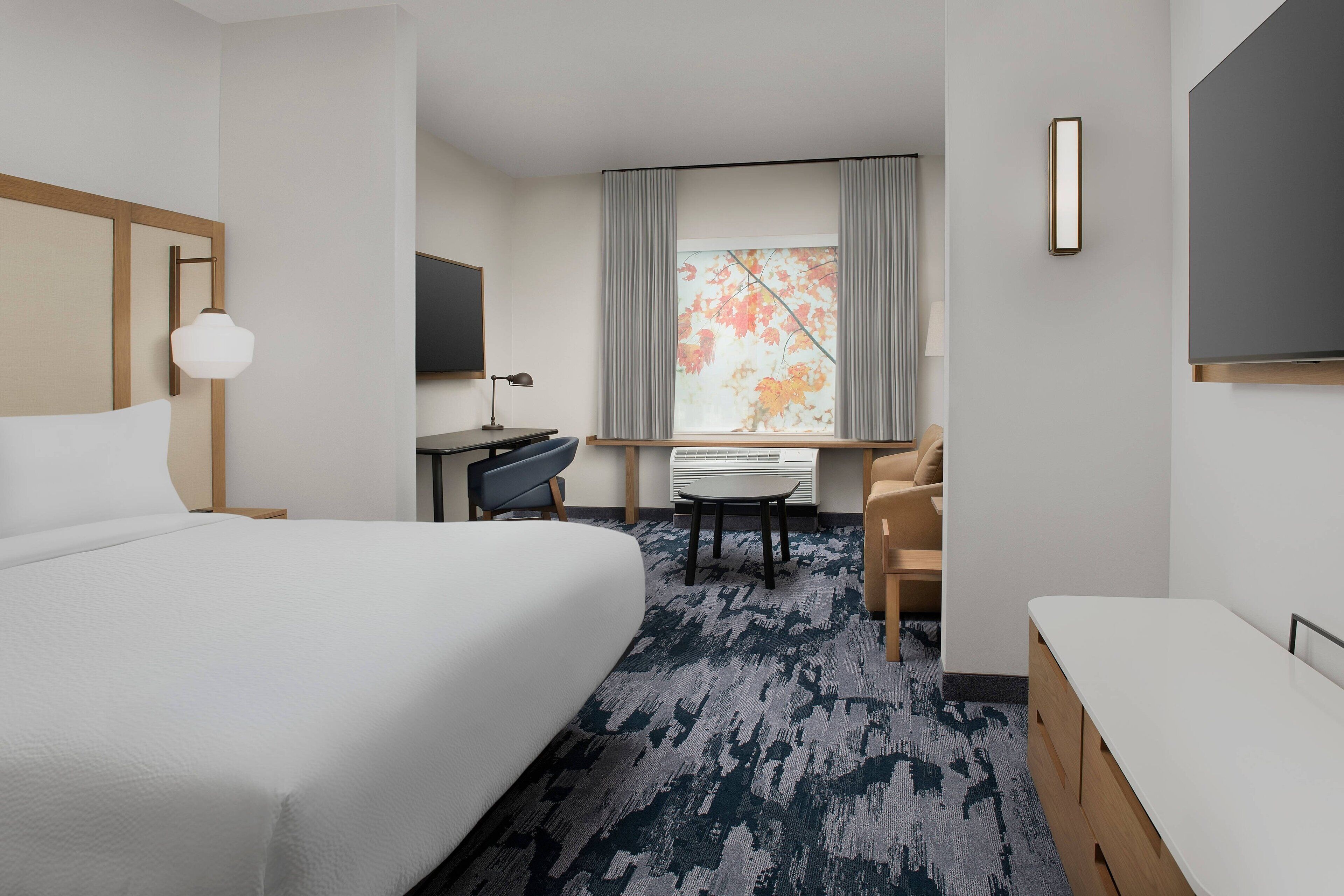A hotel room with a large bed, a desk with a chair, a TV, and a window with curtains.