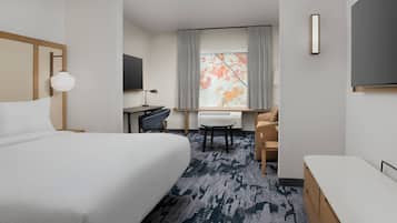 A hotel room with a large bed, a desk with a chair, a TV, and a window with curtains.