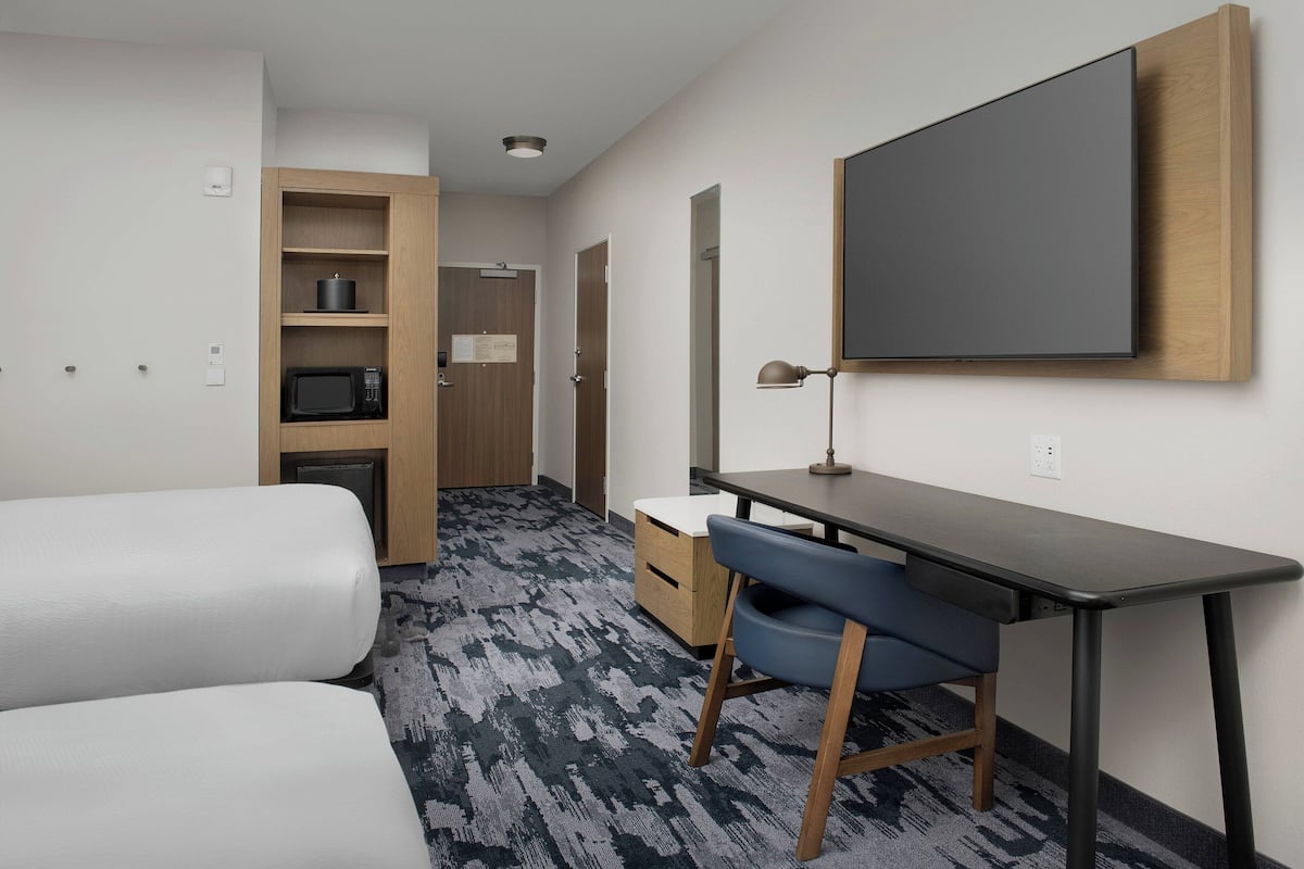 A hotel room with a bed, a desk with a chair, a flat-screen TV mounted on the wall, a microwave, and a small cabinet.