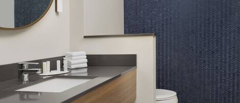 Un baño moderno con una pared de diseño oscuro, un tocador de madera, un lavamanos blanco y un inodoro.
