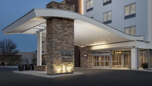Entrada moderna de hotel com fachada de pedra, um beirado curvo e uma placa de boas-vindas ao Rahrner Park.