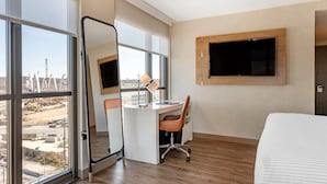 A hotel room with a large window, a desk with a chair, a bed, and a mounted TV. - Cambria Hotel Washington D.C. Navy Yard Riverfront (Washington)