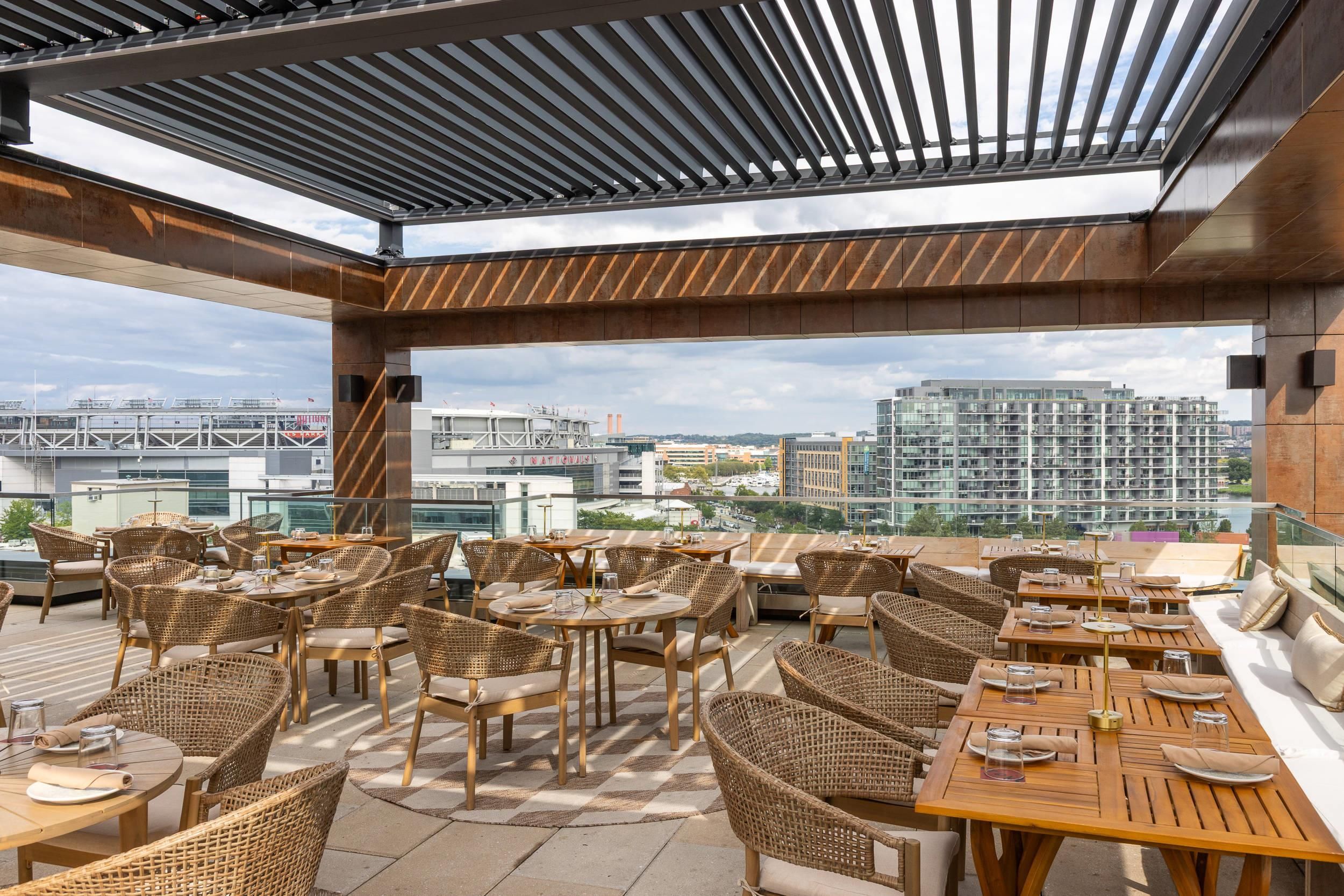 Un espacio para comer al aire libre con mobiliario de mimbre y vistas a la ciudad.