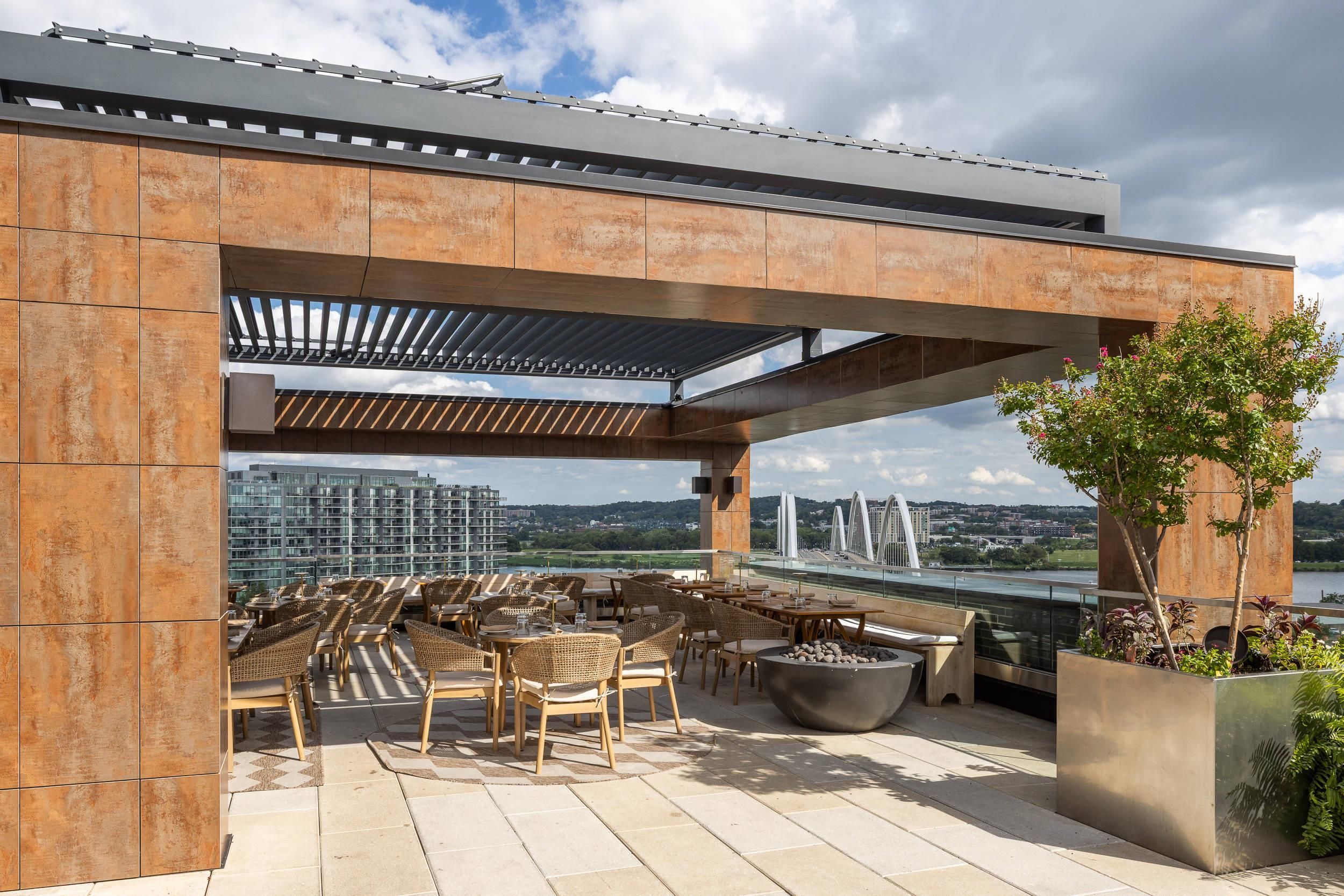 Une terrasse extérieure offrant une vue sur un pont et des bâtiments, aménagée avec des chaises et des tables en osier.