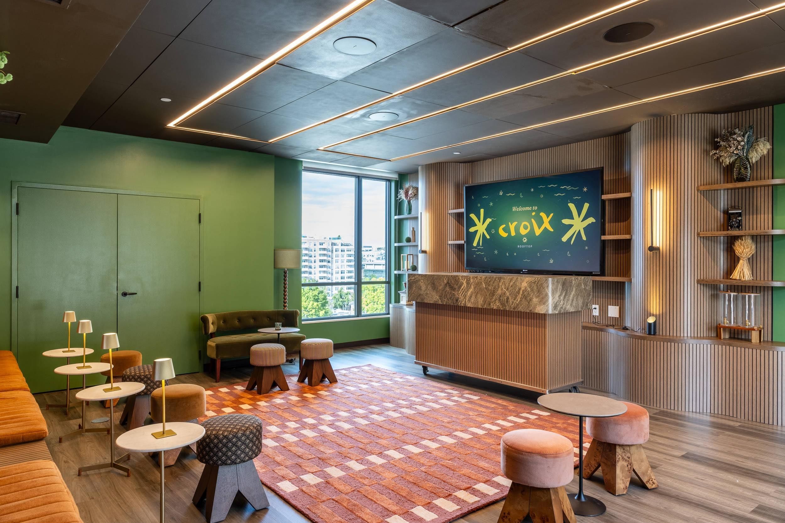 A modern lounge area with a large flat-screen TV, comfortable seating, and a view of the cityscape through large windows.