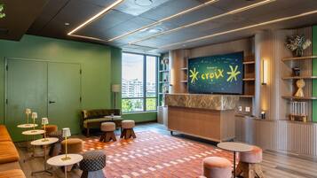 A modern lounge area with a large flat-screen TV, comfortable seating, and a view of the cityscape through large windows.