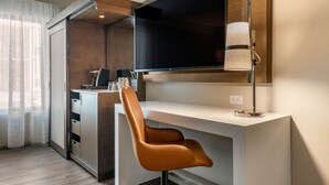 A modern hotel room with a white desk, a brown leather chair, a flat-screen TV mounted on the wall, and a lamp on the desk. - Cambria Hotel Washington D.C. Navy Yard Riverfront (Washington)