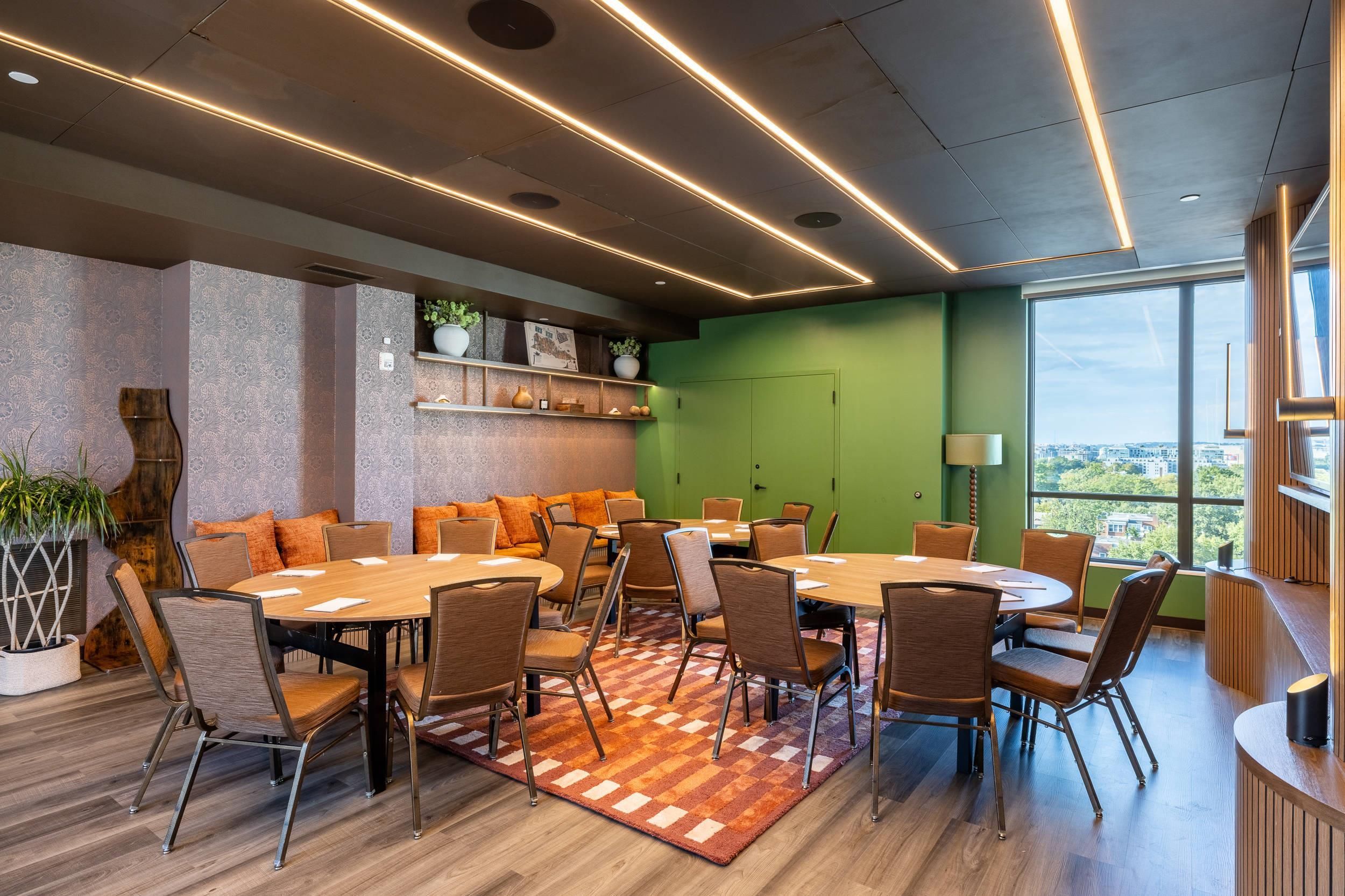 Une salle de conférence dotée d’une grande table ovale, de nombreuses chaises, d’un tapis à motifs et d’un mur d’accent vert.