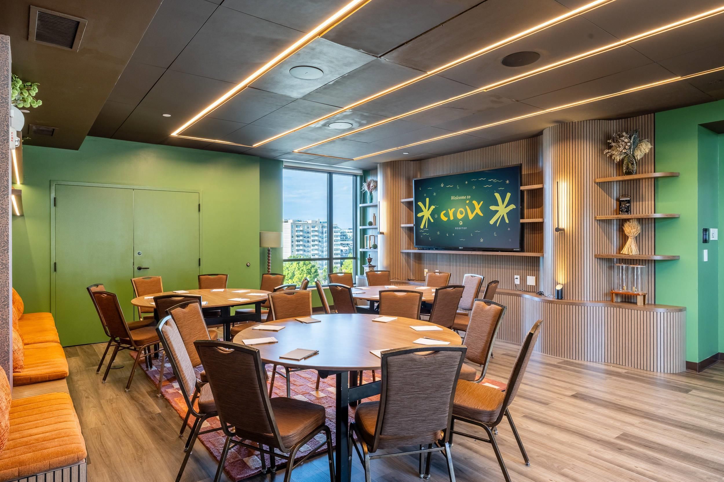A conference room with a large table and chairs, a television screen, and a view of buildings outside.