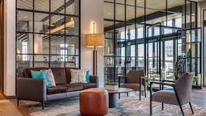 A modern lobby with a sofa, ottoman, and chairs, large windows, and a lamp. - Cambria Hotel Washington D.C. Navy Yard Riverfront (Washington)