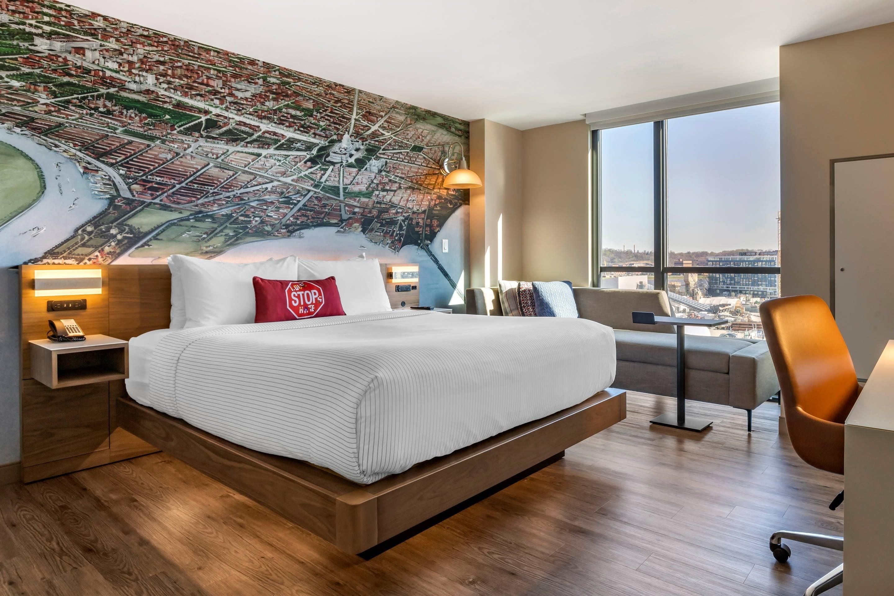 Quarto de hotel moderno com uma cama grande, um mural com vista para a cidade, e uma escrivaninha com cadeira.