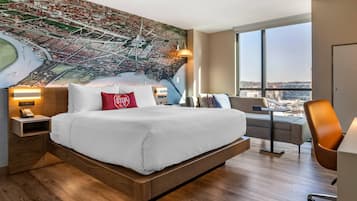 Quarto de hotel moderno com uma cama grande, um mural com vista para a cidade, e uma escrivaninha com cadeira.