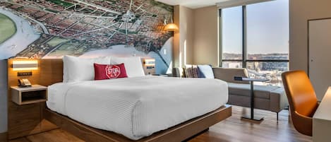 Ein modernes Hotelzimmer mit einem großen Bett, einem Stadtbild-Wandgemälde, Blick durch große Fenster und einem Schreibtisch mit Stuhl.