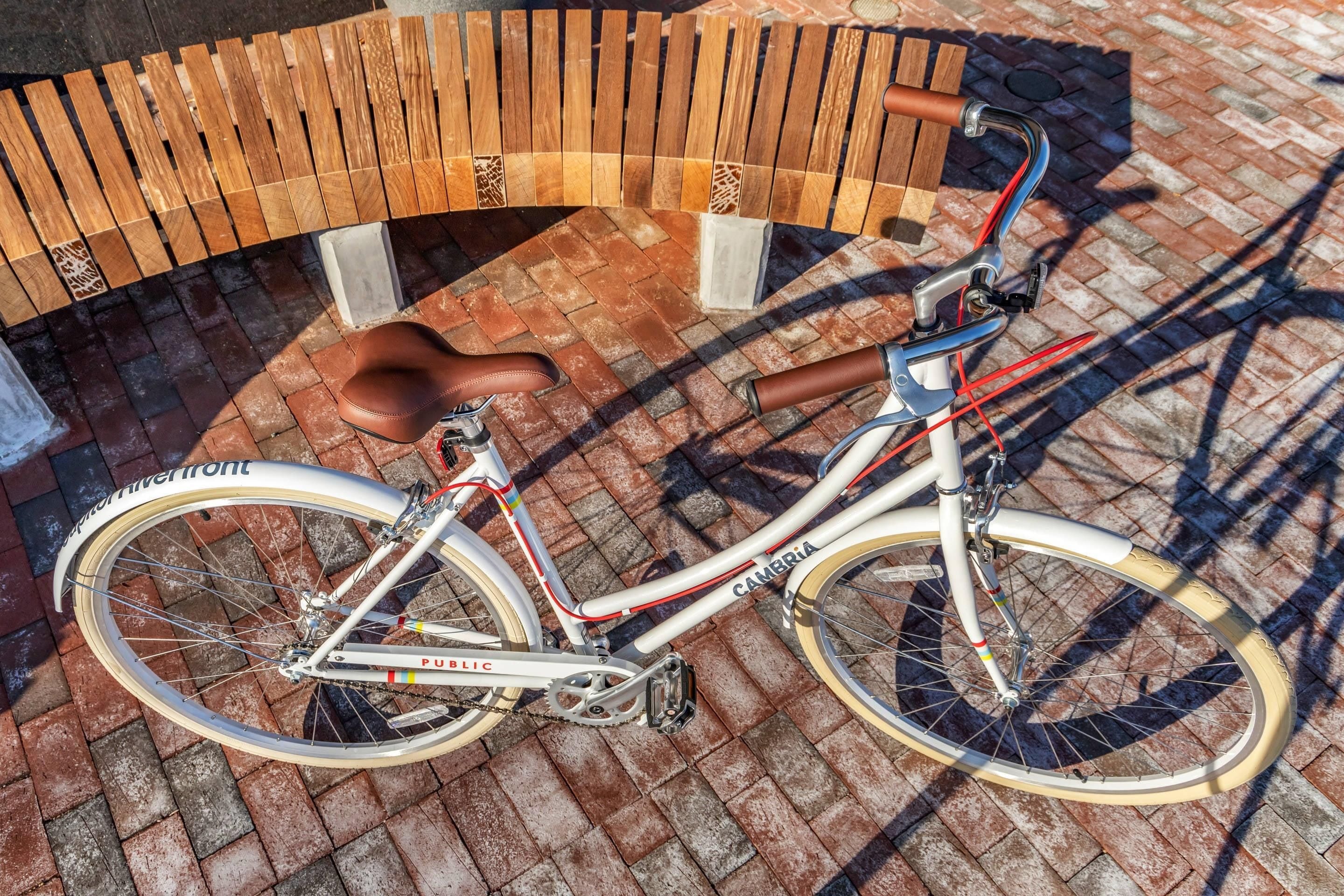 Un vélo est garé sous un banc en bois, sur un trottoir pavé de briques.