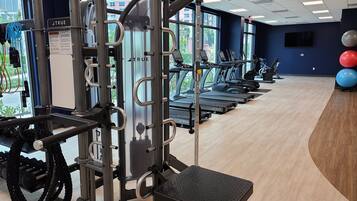 A gym with exercise equipment, treadmills, and a view of buildings outside.