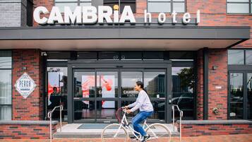 The exterior of the Cambria Hotel with a person riding a bicycle in front.