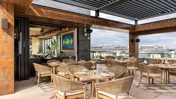 An outdoor dining area with wicker chairs and tables, a bar area, and a view of a cruise ship in the background.