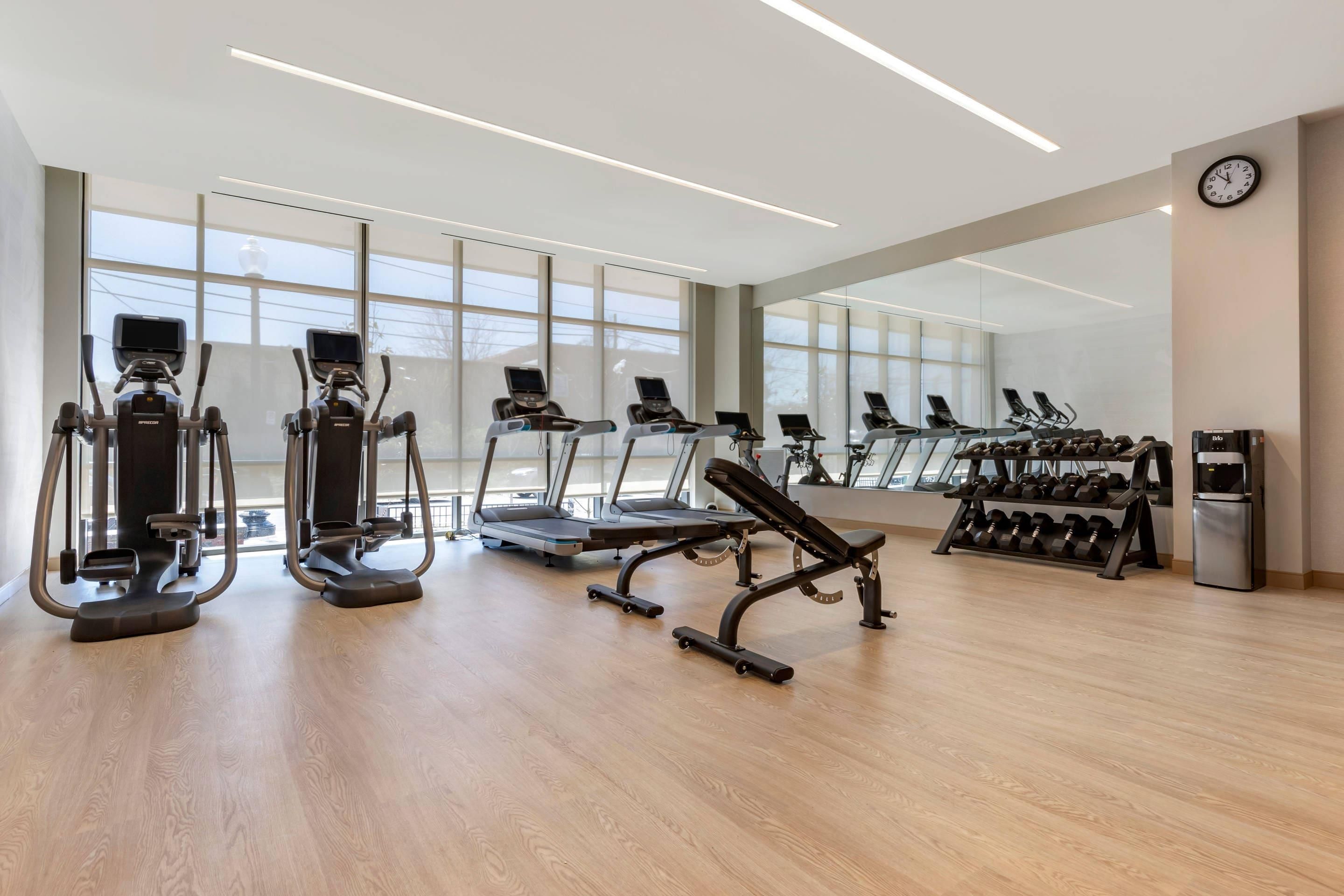 A modern gym with cardio machines, weight benches, and dumbbells.