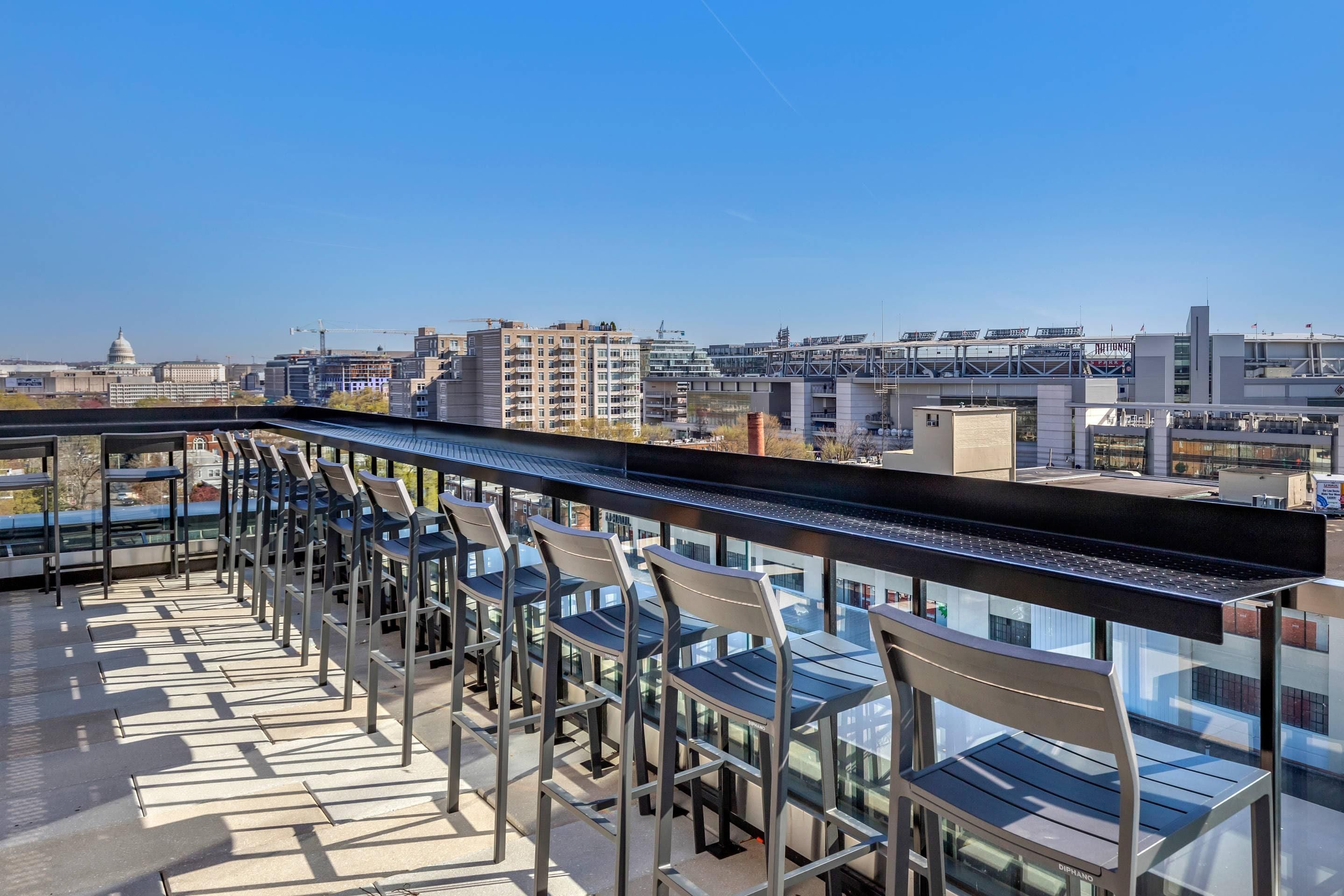 A rooftop terrace with rows of chairs and tables, offering a view of the city skyline and a bridge.