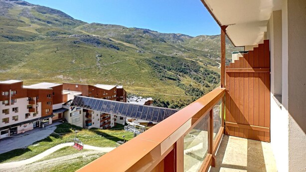 Un balcone con vista su un paesaggio montuoso, un edificio dotato di pannelli solari e una seggiovia.