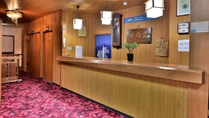 A hotel reception area with wooden paneling, a reception desk, and a red floral carpet. - Guest House Takenoya (Omachi)