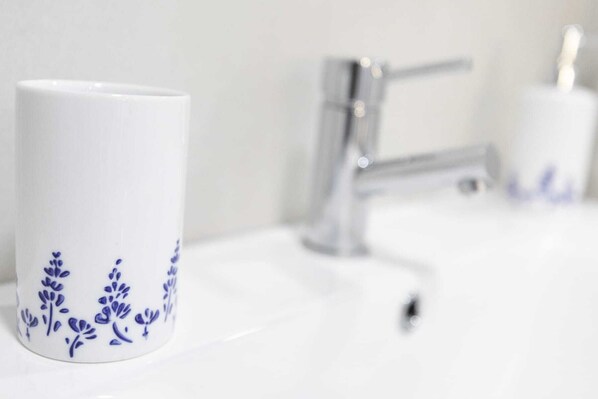Un lavamanos blanco con grifo cromado y una taza blanca con motivos florales azules.
