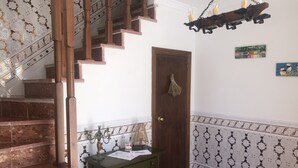 Un escalier avec des rampes en bois, une porte en bois ornée d’une frange, une petite armoire verte et des carreaux muraux à motifs.
