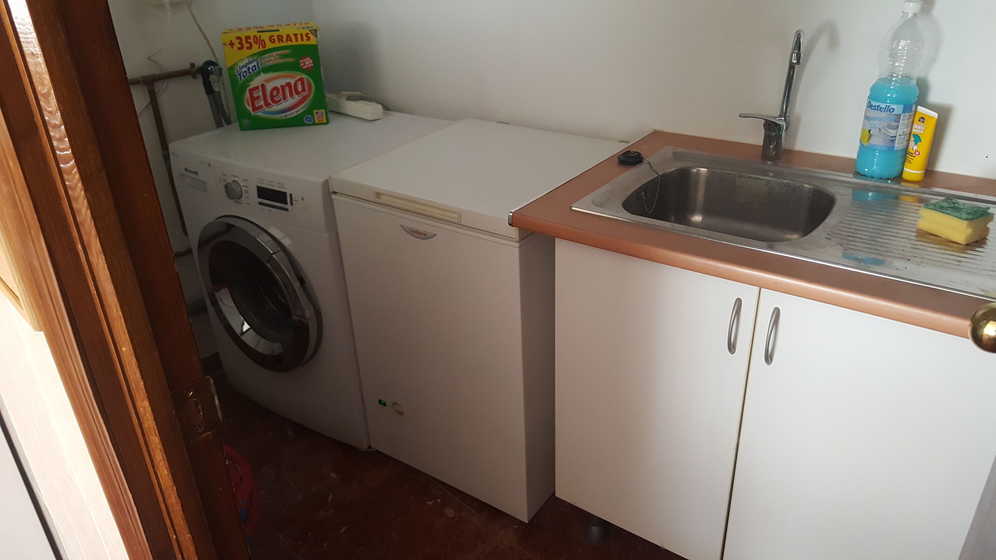 Ein kleiner Waschraum mit Waschmaschine, Trockner, Spüle und einer Flasche Waschmittel sowie einer Packung Waschpulver.