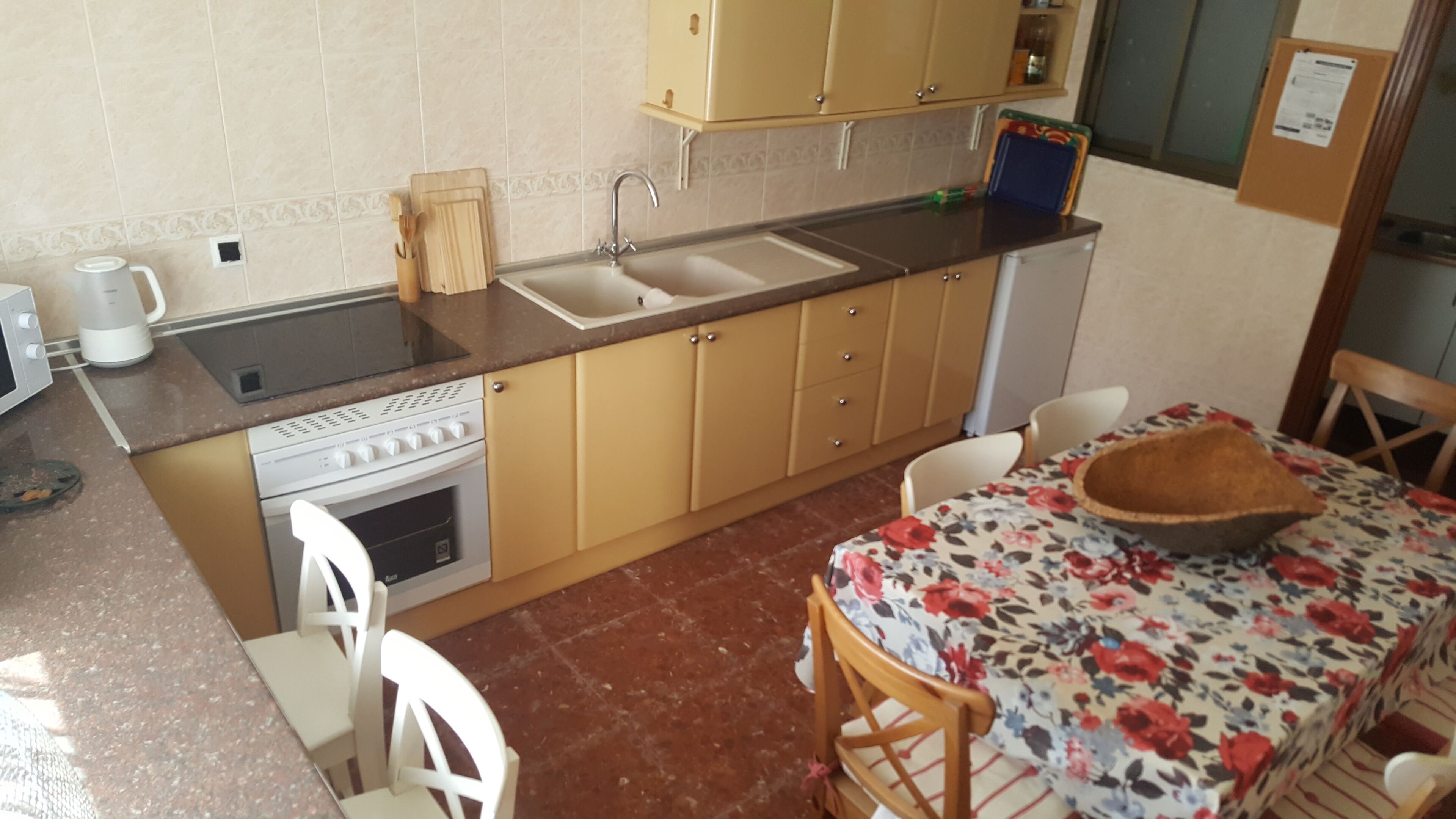 Cocina compacta con estufa, lavamanos y armarios de madera. Hay una mesa de comedor con sillas y un cuenco decorativo.