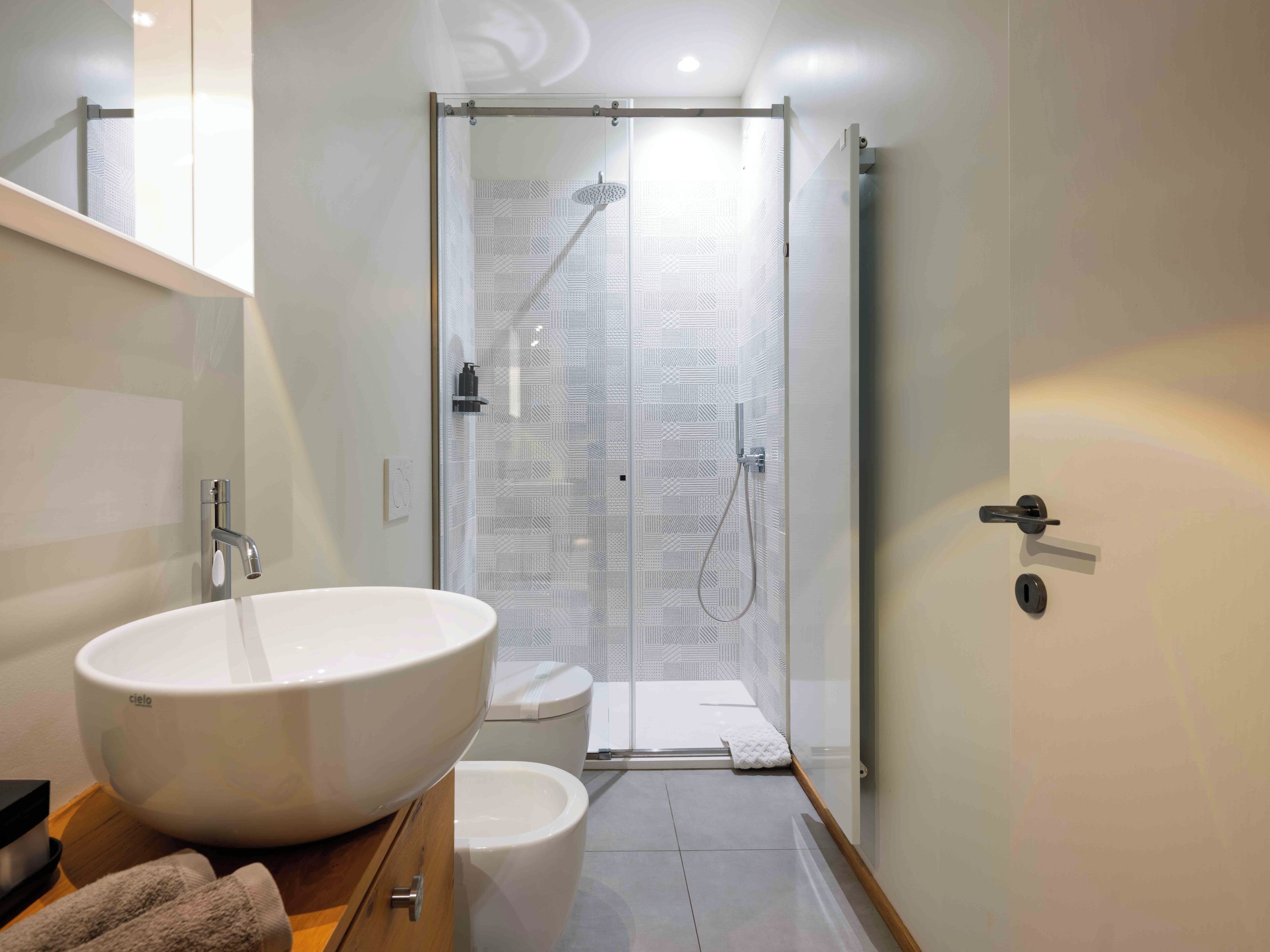 Een moderne badkamer met een grote witte wastafel, een toilet en een douche met glazen wanden.