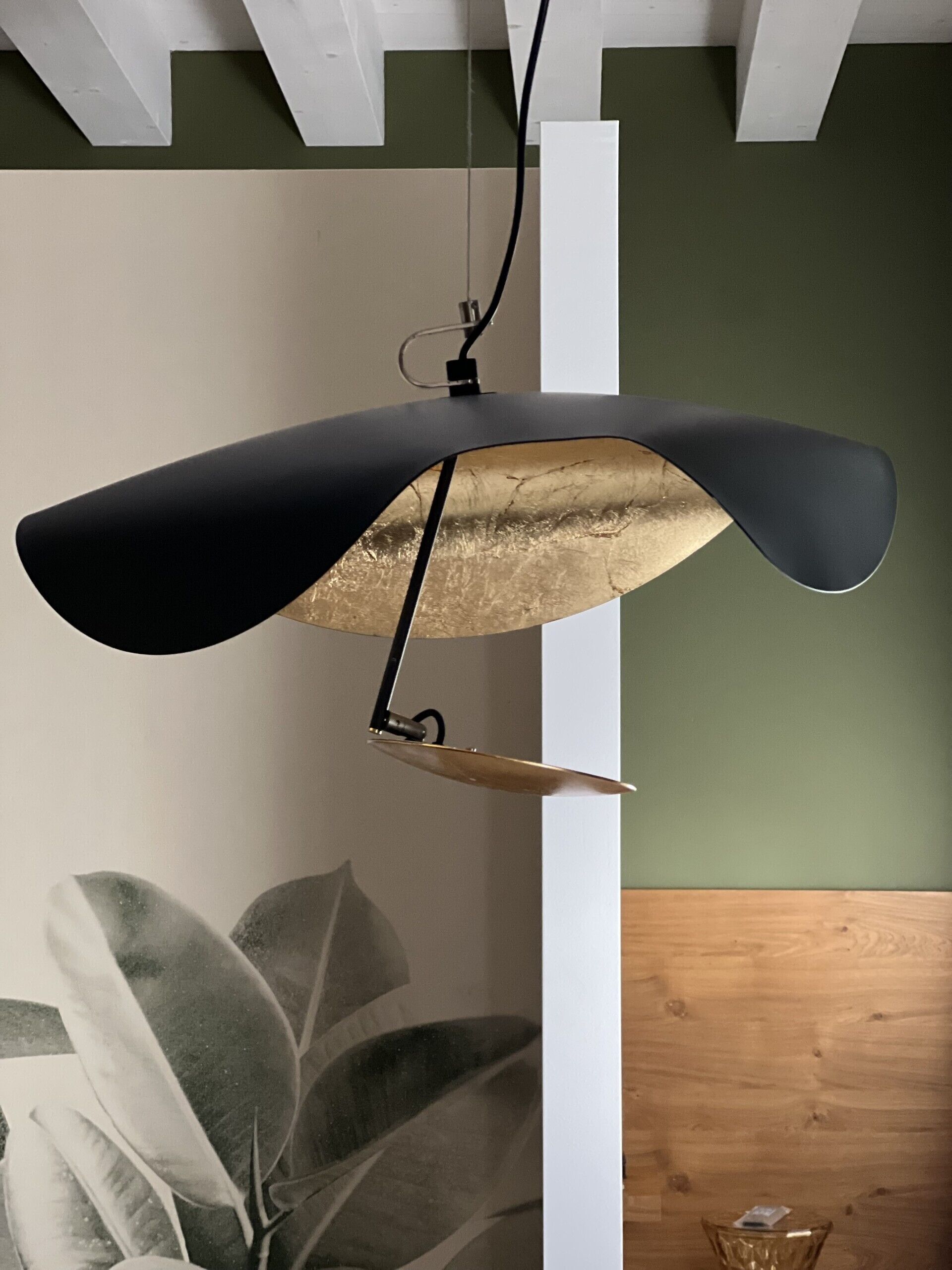 A pendant light with a black shade and gold interior, hanging from a white ceiling.