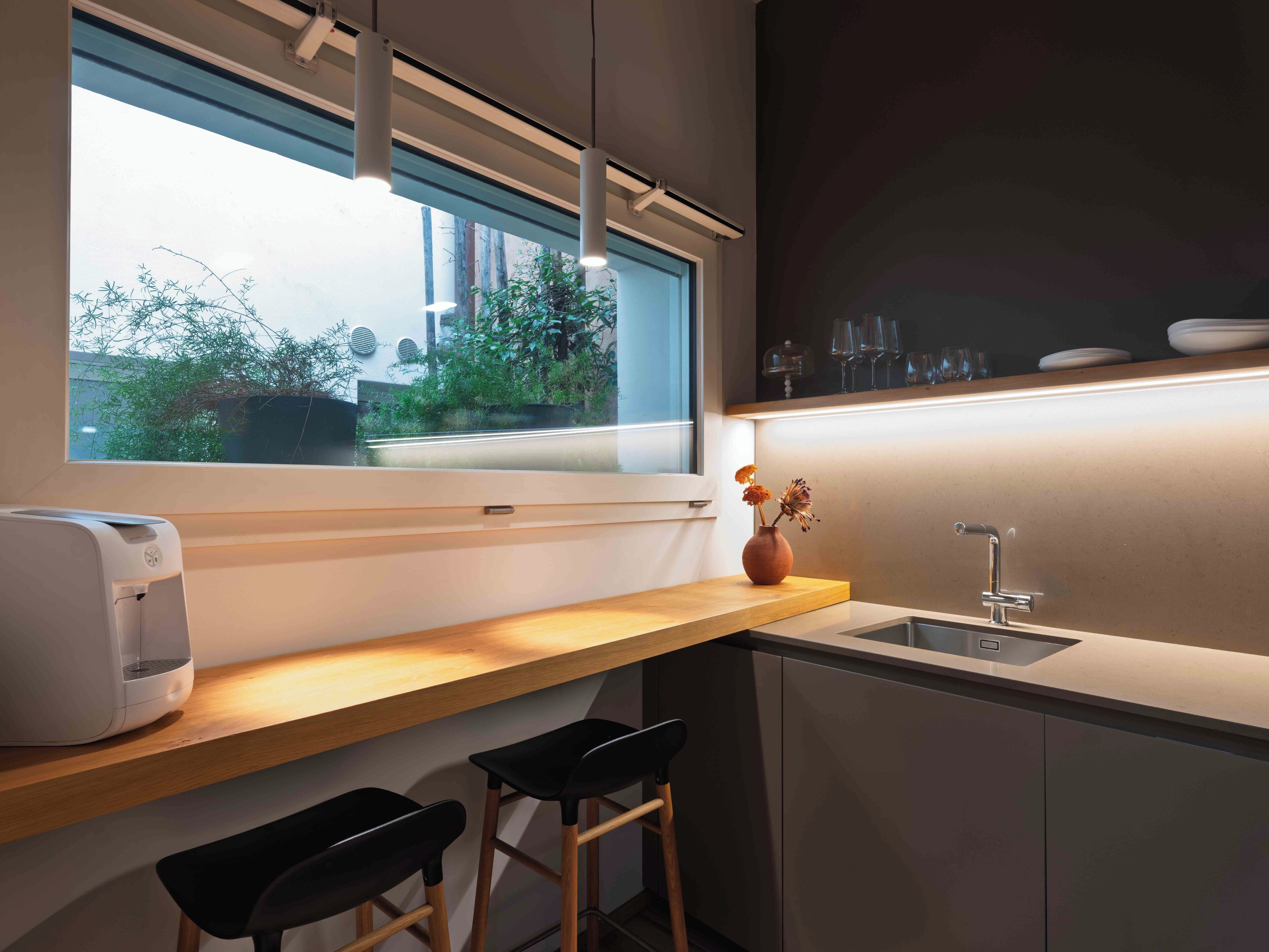 A modern kitchen with a window, a sink, a countertop, and two bar stools.