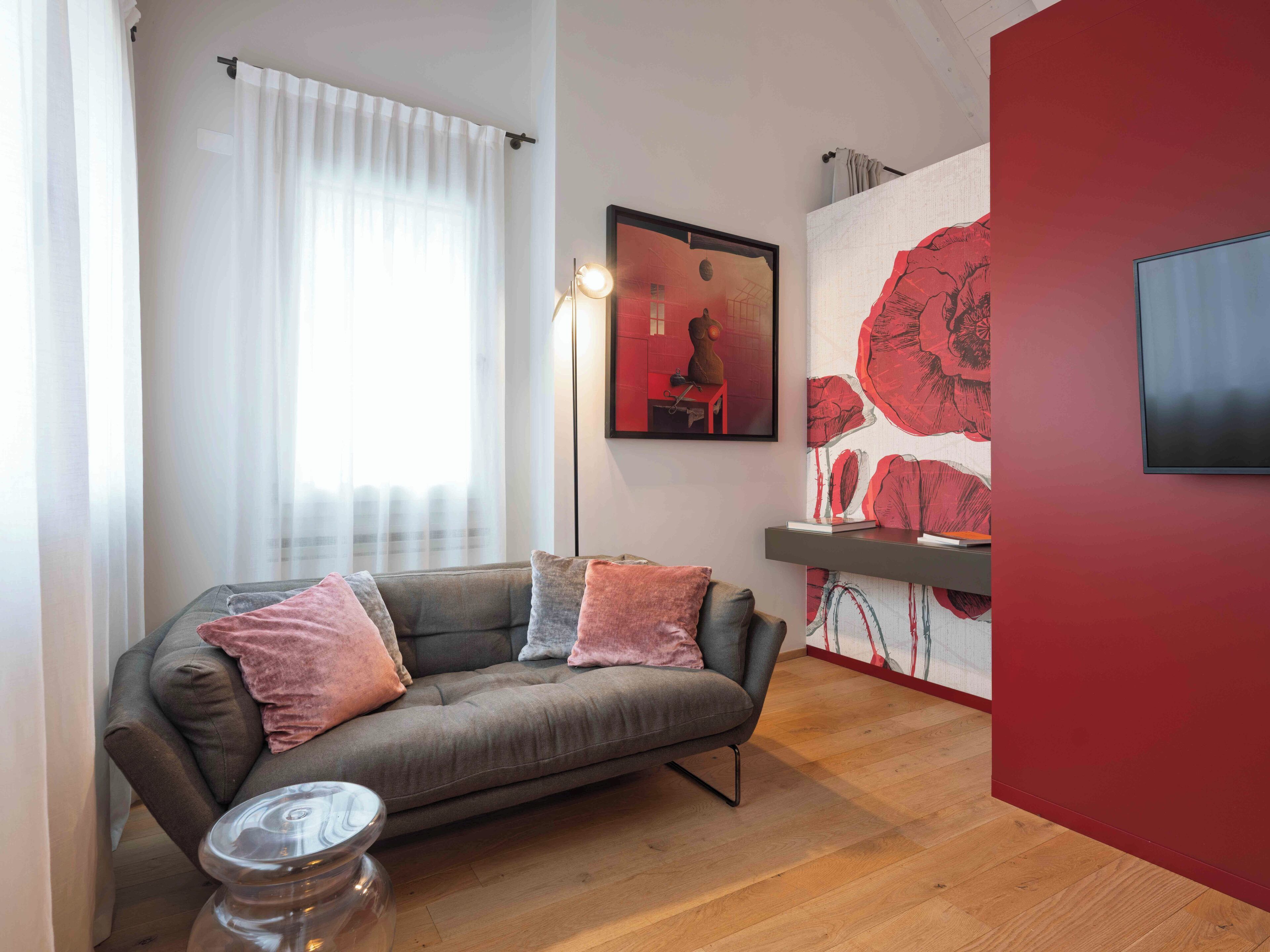 Ein modernes Wohnzimmer mit einem grauen Sofa, einem kleinen Beistelltisch, einer roten Akzentwand und einem gerahmten Kunstwerk.