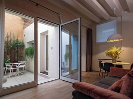 Un interior moderno con un puerta corredera de vidrio que da a un balcón, un sofá, una mesa con sillas y un jarrón decorativo con flores.