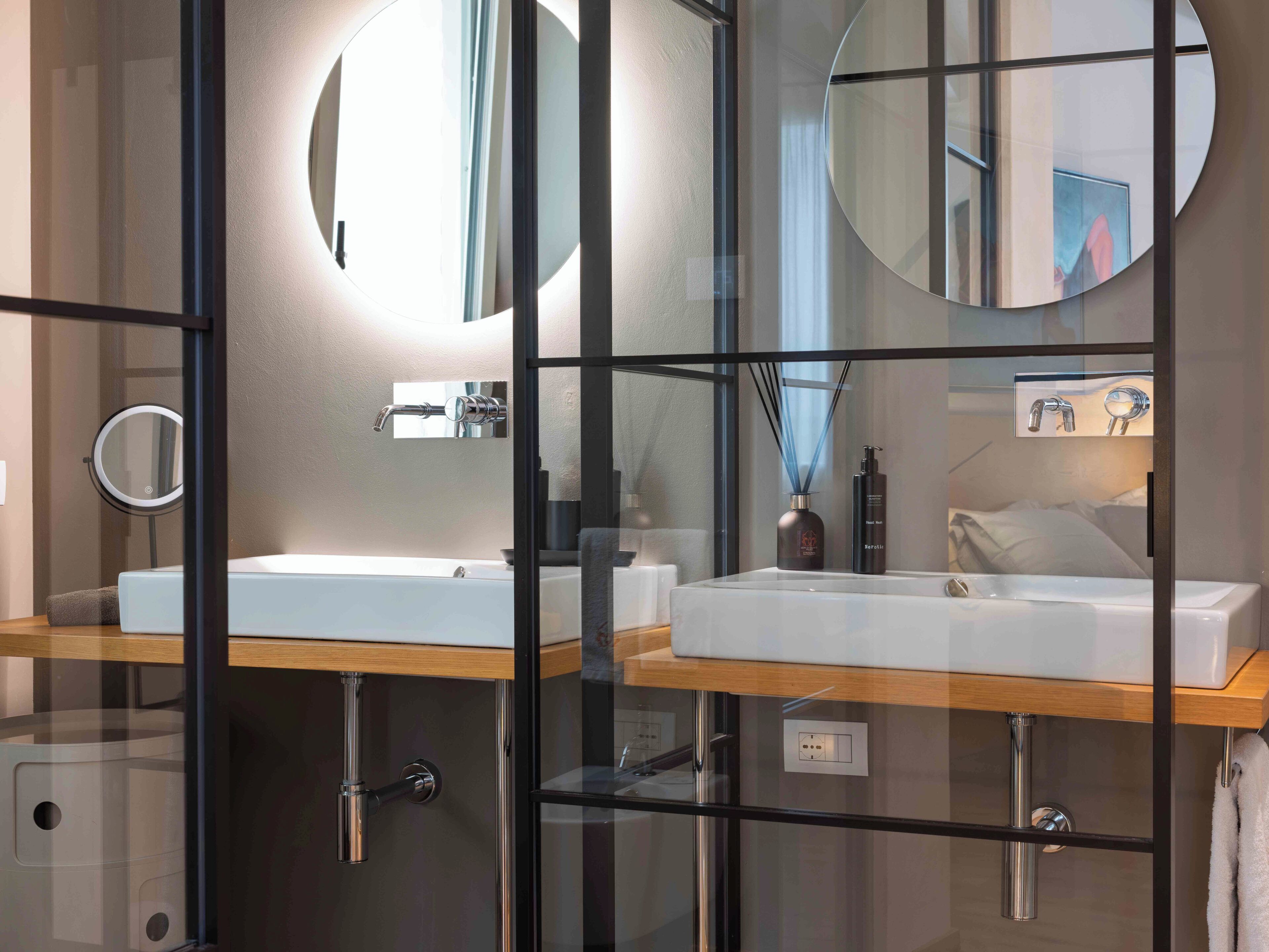 Une salle de bain moderne avec deux lavabos, un miroir et une cloison en verre.