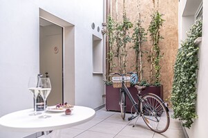 Un espacio exterior reducido con una bicicleta, una mesa con una copa de vino y una puerta con un cartel de prohibido fumar.