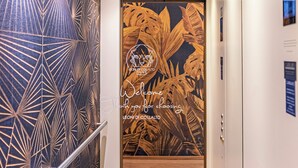 An elevator interior with geometric wall patterns, a wooden floor, and a door with a tropical leaf design. - Leoni di Collalto Palace (Treviso)