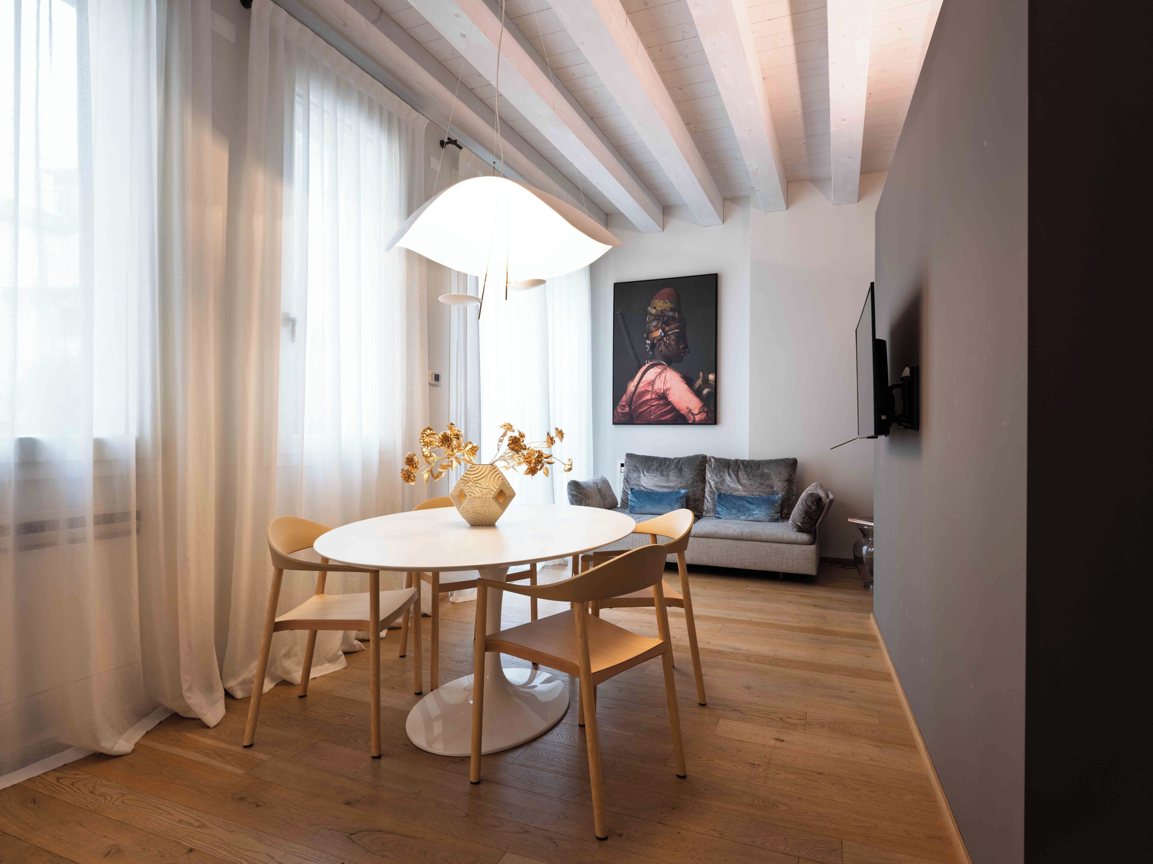Un coin repas avec une table ronde, des chaises, un vase contenant des fleurs séchées, un canapé avec des coussins et un tableau accroché au mur.
