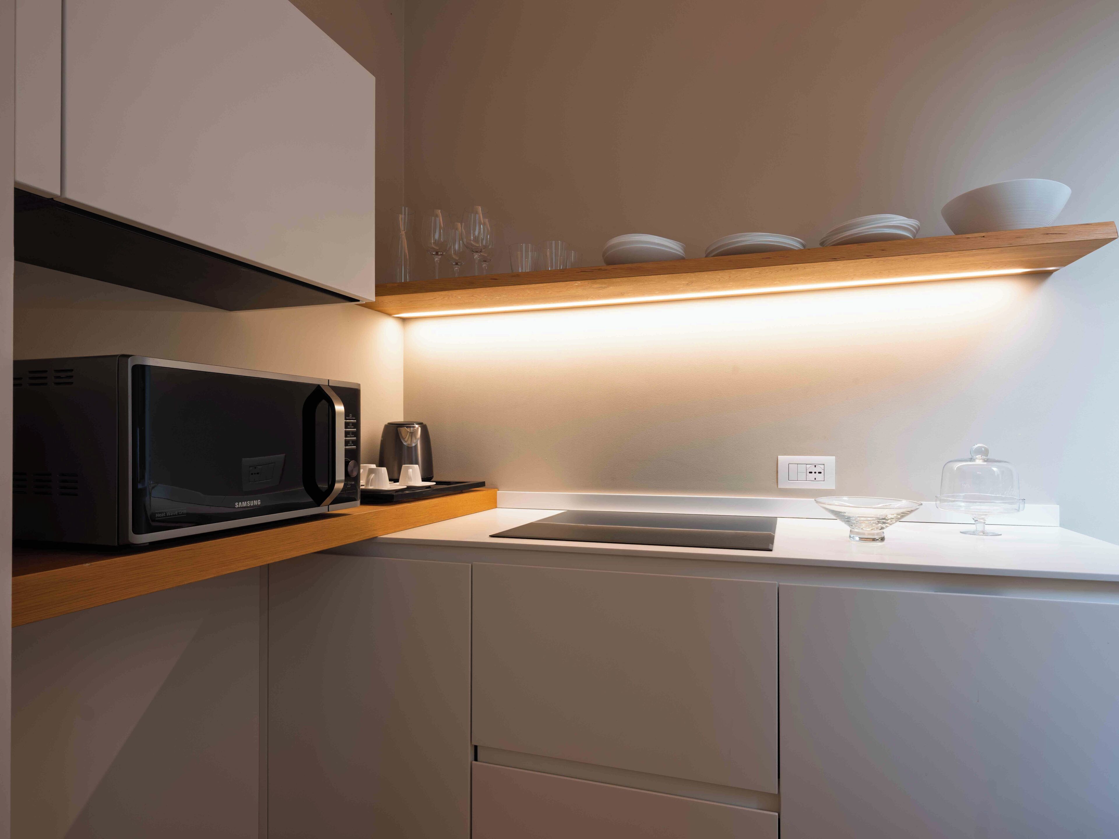A modern kitchen with a microwave, coffee maker, and a shelf with bowls and glasses.