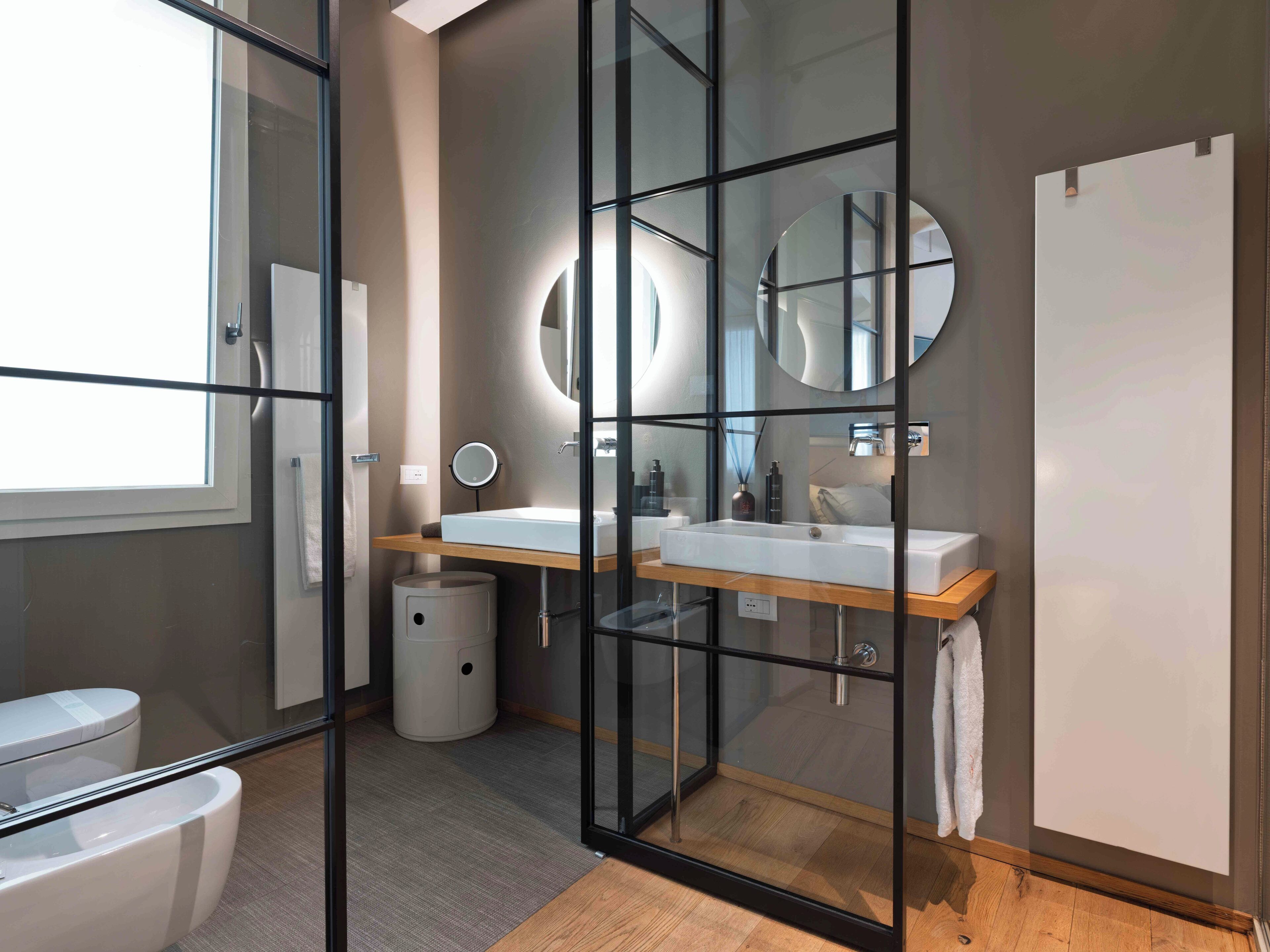 Un baño moderno con mampara de vidrio, dos lavamanos, un espejo y un inodoro.