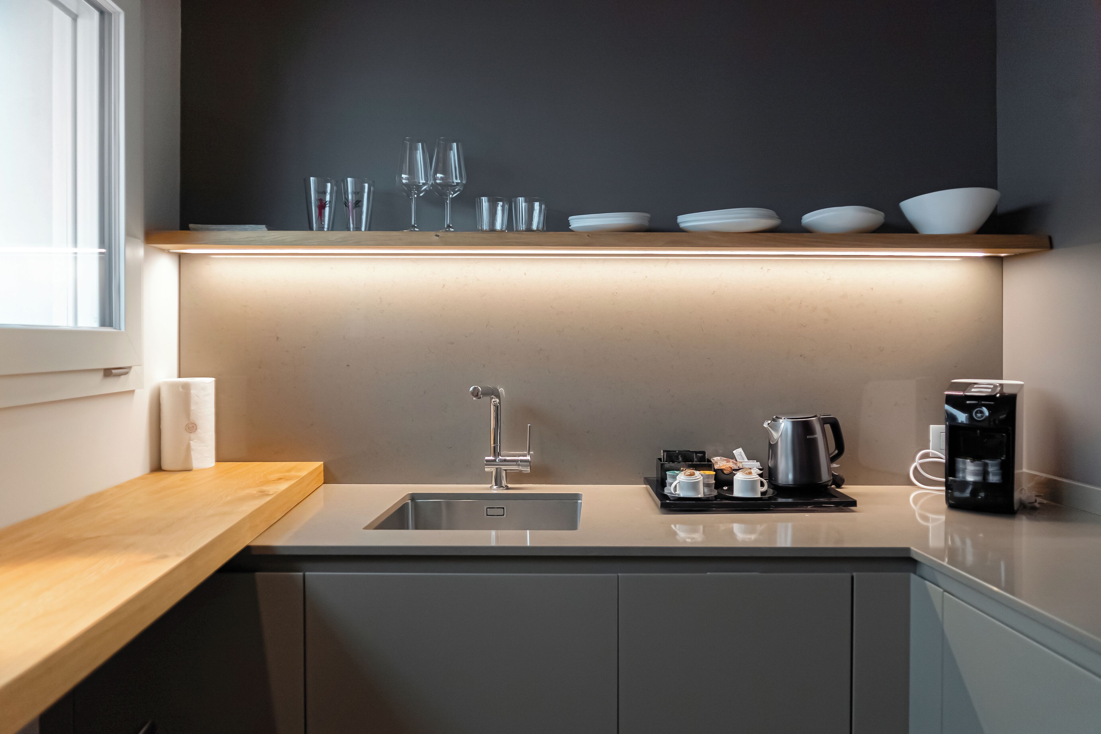 Eine moderne Küche mit integriertem Spülbecken, einer Holz Arbeitsplatte und einem Regal über dem Spülbecken, das Glaswaren und Schüsseln beherbergt.