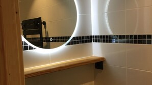 Ein Badezimmer mit einem schwarzen Waschbecken, einer Holzablage und einem Spiegel mit runder Beleuchtung.
