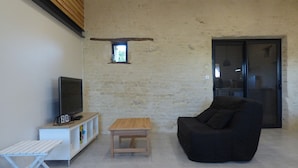 A modern living room with a flat-screen TV on a white stand, a black sofa, a wooden coffee table, and a small shelf with various items.
