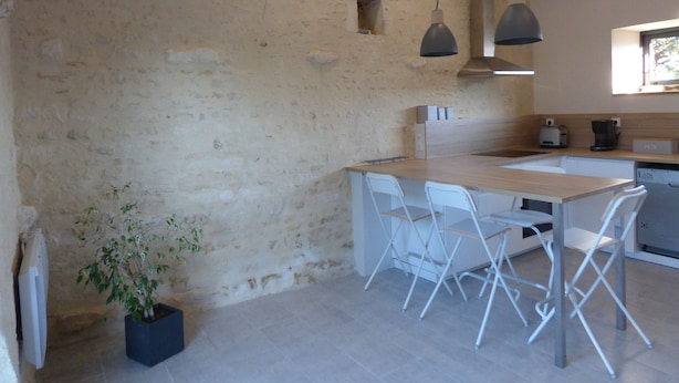A kitchen with a wooden island, white chairs, hanging pendant lights, and a potted plant.