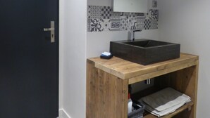 A bathroom with a dark door, a wooden vanity with a sink, a mirror, patterned tiles, and a small shelf with towels.