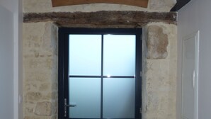 A stone wall entrance with a wooden sign above a black door.
